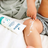 Application de la crème Biolane sur la jambe d’un bébé à la peau sensible